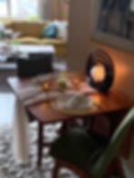 Mid-century modern drop-leaf table set for two with amber votives, a cheesecloth runner, cloth napkins, and a glowing black sculptural lamp, tucked in a cozy apartment pass-through for date night.