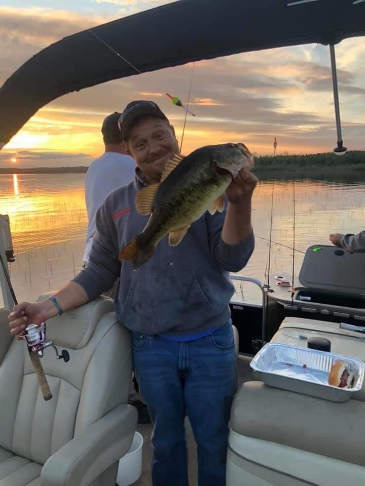 Angler shows off largemouth bass on pontoon boat during sunset on Kitchi Lake, part of Minnesota's C