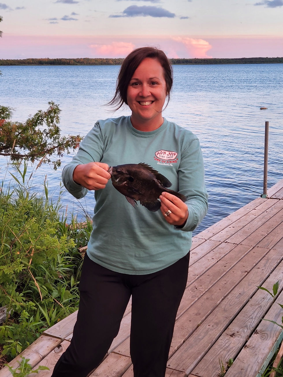 Smiling woman holding a freshly caught bluegill on the dock at Kitchi Landing Resort, with Cass Lake