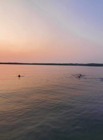 Swimmers enjoy a peaceful sunset over Kitchi Lake at Kitchi Landing Resort, Minnesota.