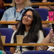 Conference attendee seated in a lecture theatre listening to a presentation.