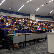 Wide view of a conference presentation with attendees seated in a lecture theatre.
