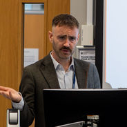 Presenter speaking beside a display screen during a workshop session.