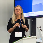 Presenter speaking into a handheld microphone in a lecture theatre.