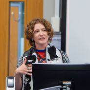 Presenter standing beside a presentation screen and speaking during a workshop session.