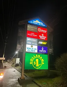 illuminated pylon sign on a sidewalk with various business logos on it.webp