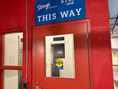 Blue Wayfinding Sign above a red door stating Stong's Market This Way