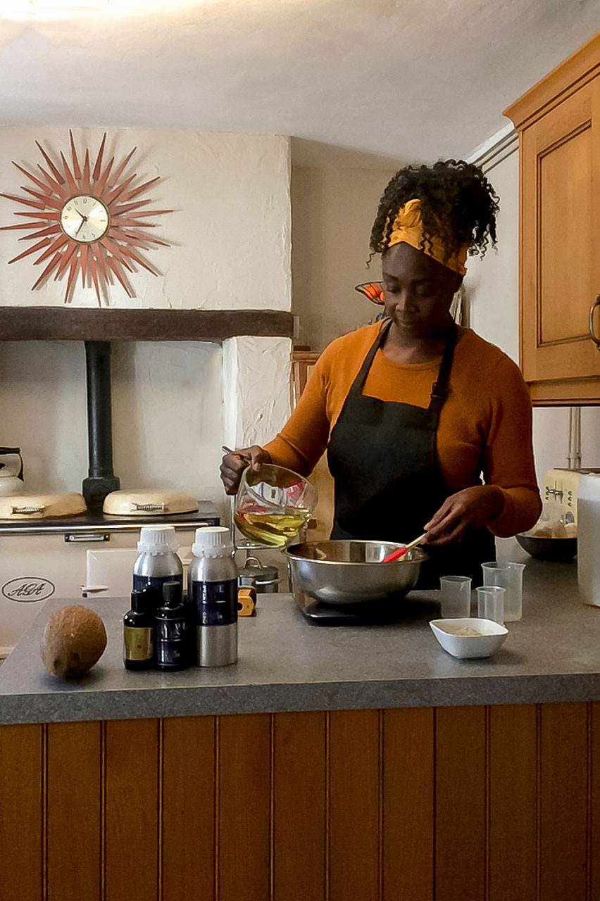 Black woman pouring melted candle wax into stainless steel down in a kitchen with vintage Aga in the background