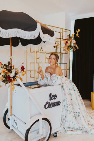 Woman in floral dress eating "Ice Cream" from a white cart.