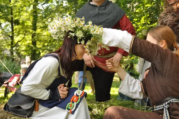 Young woman receiving a flower crown made of camomile and wild herbs during a traditional Slavic midsummer celebration, symbolizing love and protection.