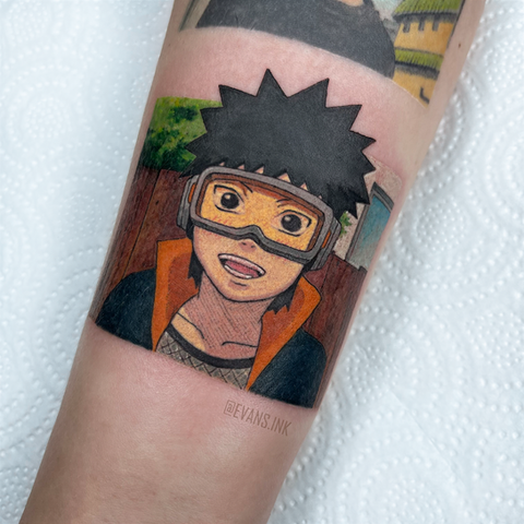 Tatuaje a color del joven Obito Uchiha con gafas de Naruto en el antebrazo por Yana Evans