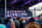 DJs perform for a crowd on a stage with a large LED screen.