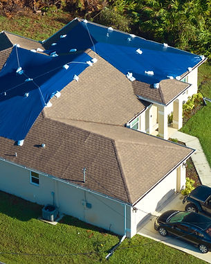 Aerial view of damaged in hurricane Ian house roof covered with blue protective tarp again