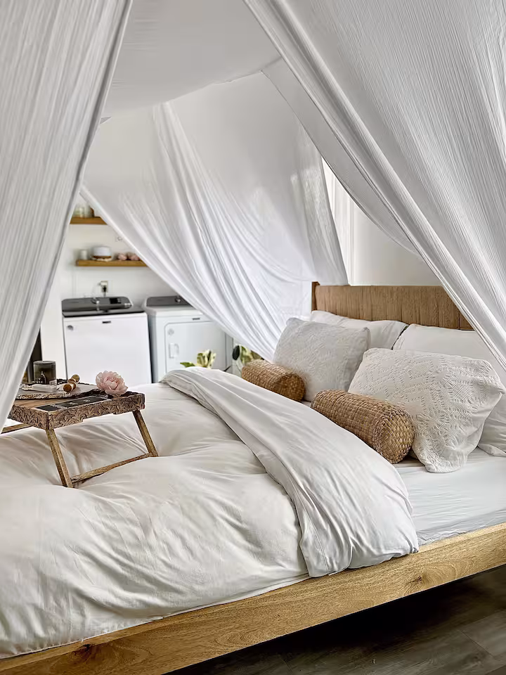 A chic bedroom setting with white canopy curtains, warm-toned bedding, and bohemian accents, creating a soft and inviting photography backdrop