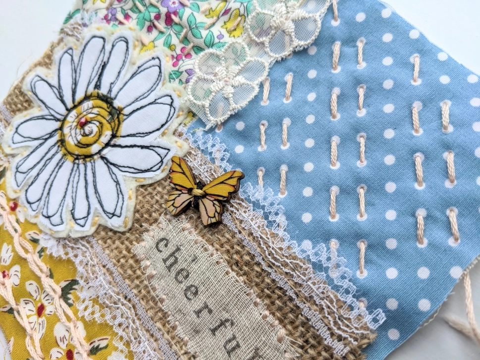 Slow stitch large white daisy on hessian strip with florals, blue and lacy materials as the background