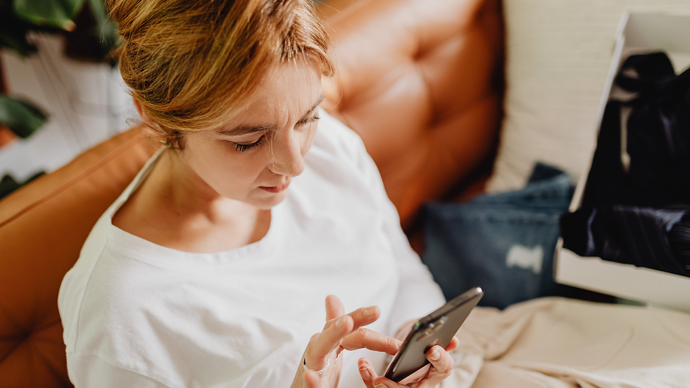 Femme assise sur un canapé regardant son téléphone, l’air préoccupé, illustrant la recherche de produits ménopause et le marketing “menopause tech”