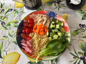 une assiette quinoa, crudités et poulet sur une table avec nappe citrons et olives