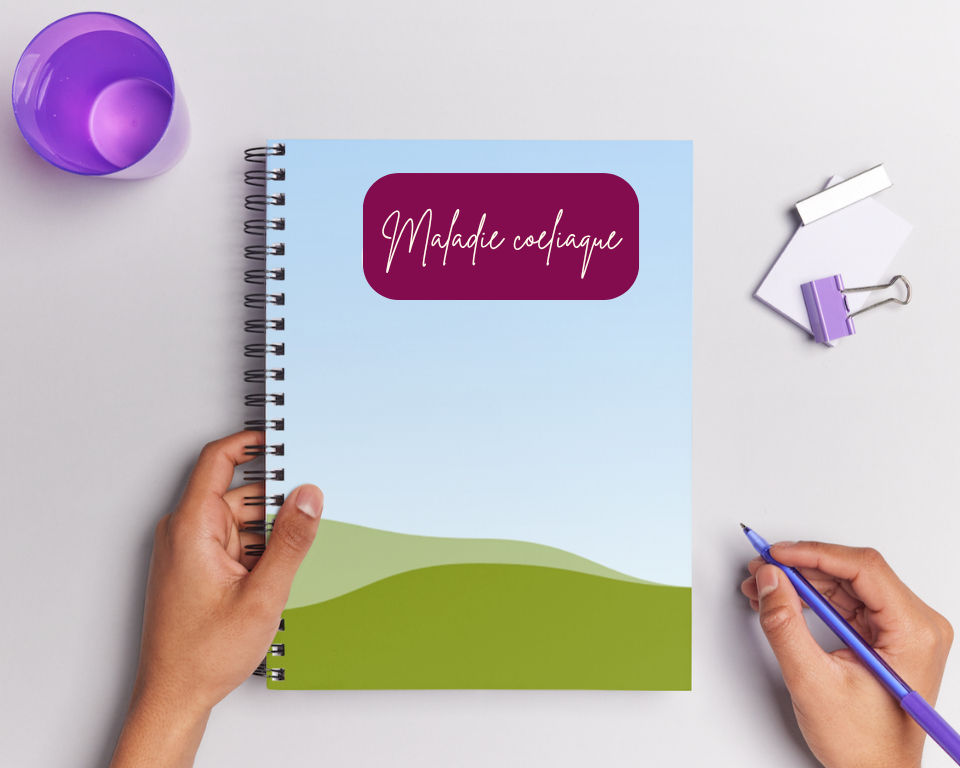 Carnet sur une table avec le mot “Maladie cœliaque” sur la couverture, posé près d’un stylo et d’accessoires de bureau.