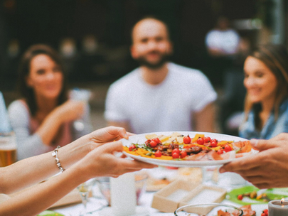 Group of friends having dinner where one person is passing a plate full of food to another.