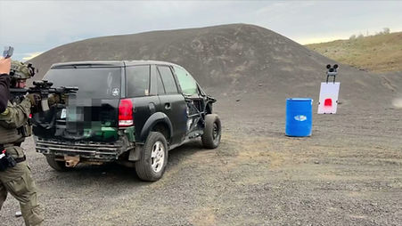 Shooters in tactical gear fire from behind a vehicle at a moving target, three pop-up targets rise and drop, and a turning target turns to face the shooter.