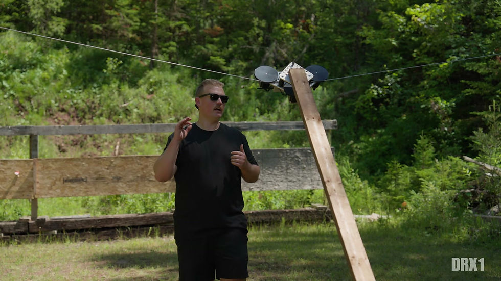 The X1 target carriage hanging from the overhead cable with a 2x4 of target lumber bolted to it, a man standing alongside on the range