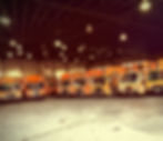 Multiple Orange Trucks parked in the garage front facing in a circle. Dim Lighting.