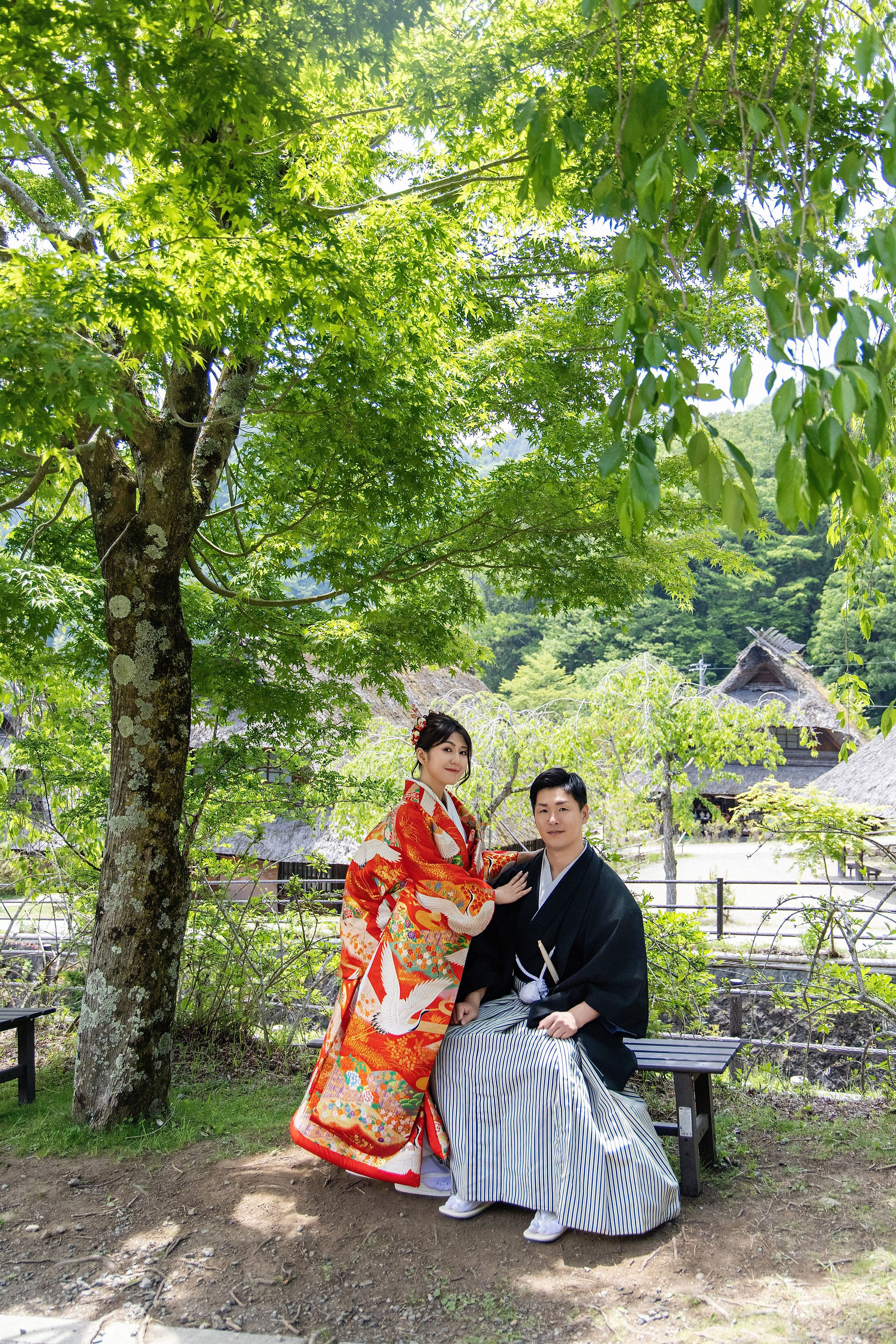 Bride and groom wearing traditional Japanese wedding kimono at Saiko Iyashi no Sato Nenba with Mount Fuji behind them.