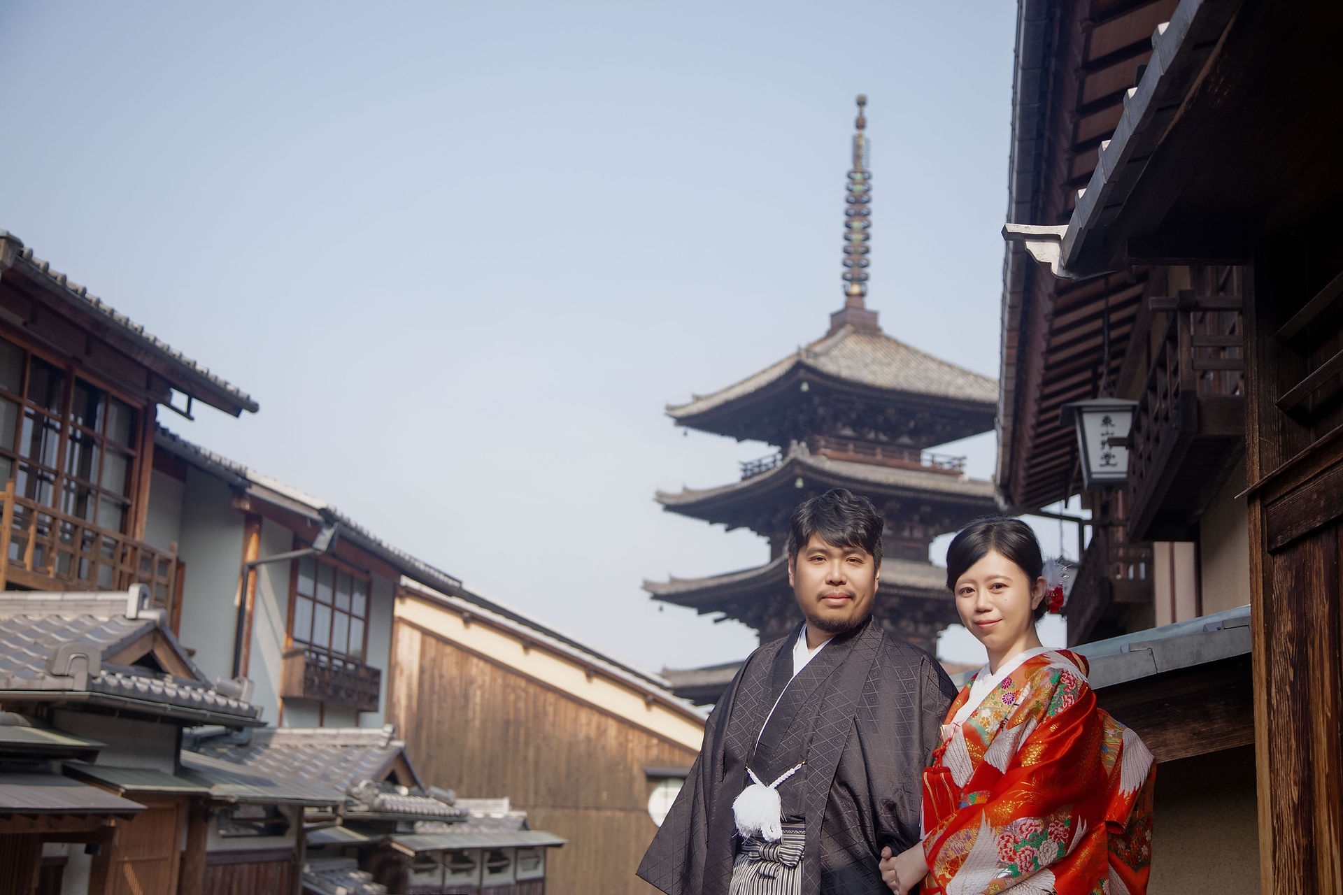 Couple wearing traditional wedding kimono standing along a historic Kyoto street with Yasaka Pagoda in the background.