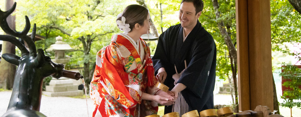 Couple performing a traditional purification ritual at a shrine before their Shinto wedding ceremony in Kyoto.