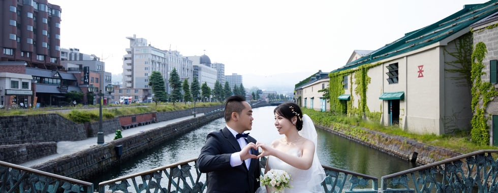오타루 운하의 눈景과 역사적인 거리 프리웨딩 촬영를 배경으로 서로를 바라보는 신랑신부 사진.