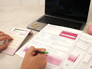 Hands use a pink calculator and pen over Octopus Energy forms beside a laptop, coins, and a pink mouse on a desk.