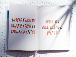 Open book with colorful text: "Wish for it, hope for it, dream of it" and "But by all means do it" on polka dot background. Shadows present.