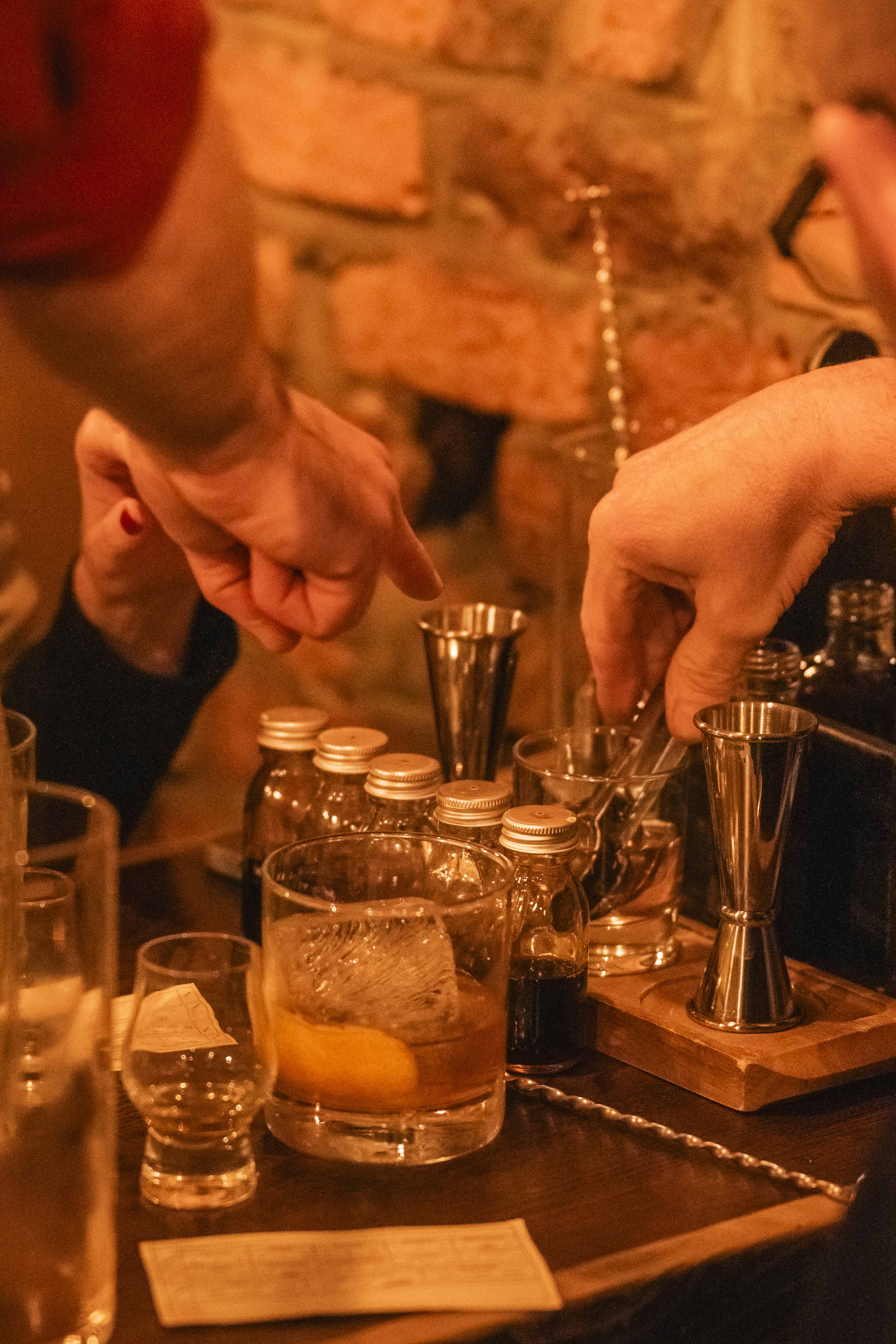 cocktail equipment for making the perfect old fashioned. The image shows a selection of 5 glass dropper bottles containing different bitters, cocktail jigger, syrups and tasters of the different whiskeys, 