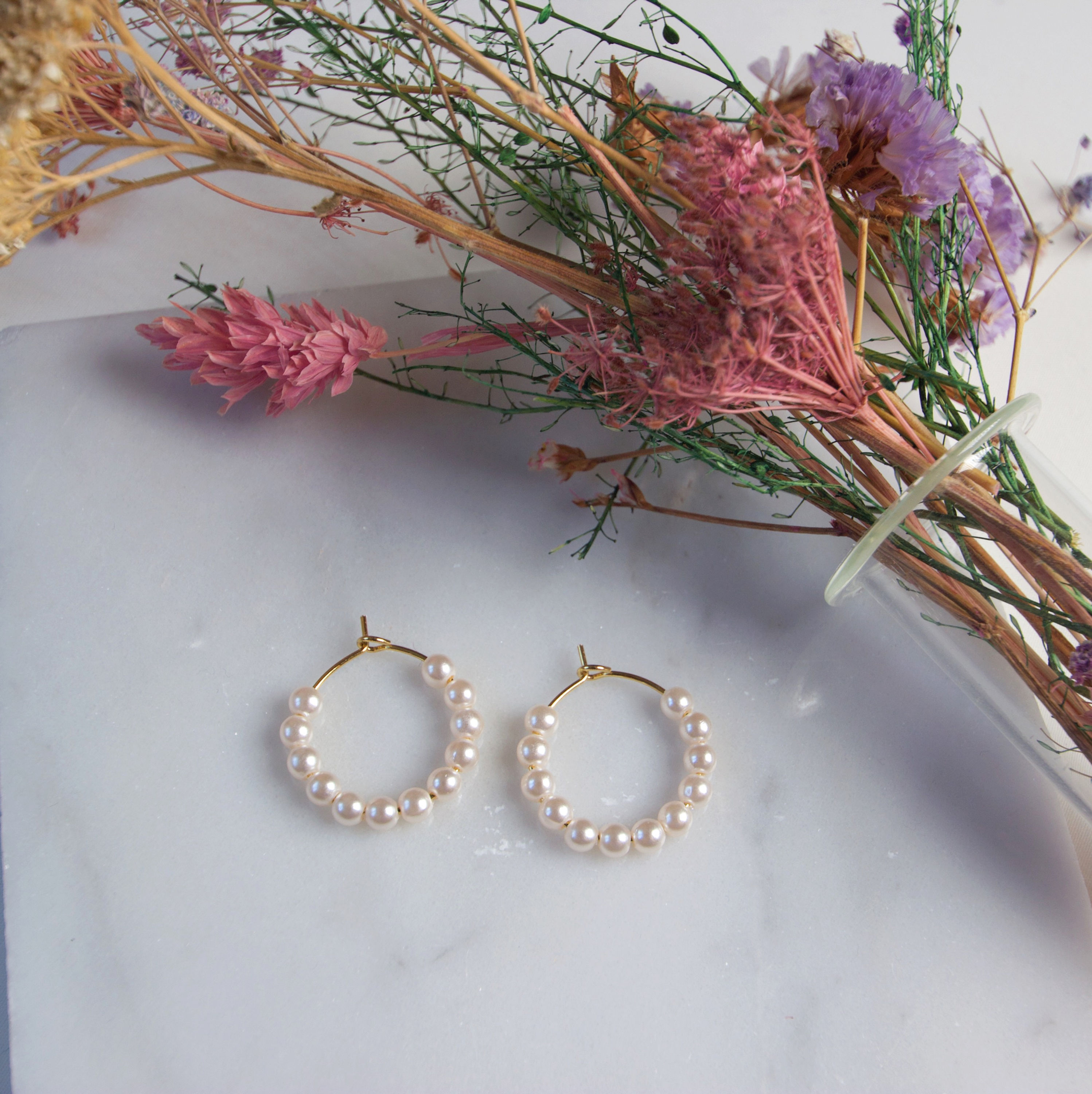 Hvide perler og guld hoops - smukke øreringe på hvid marmors overflade og tørre blomster.