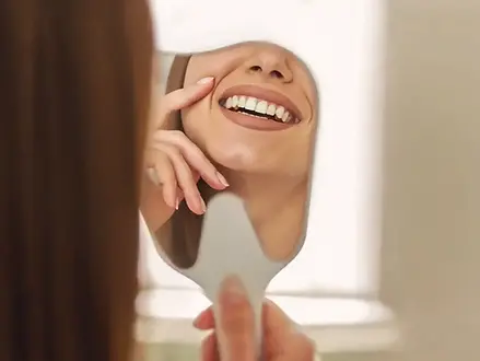 Woman looking at her smile in a mirror representing cosmetic dentistry at White Dental.
