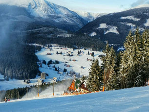 Skipiste in Tsjechië met besneeuwde bergen, naaldbossen en een winters bergdorp in het dal.