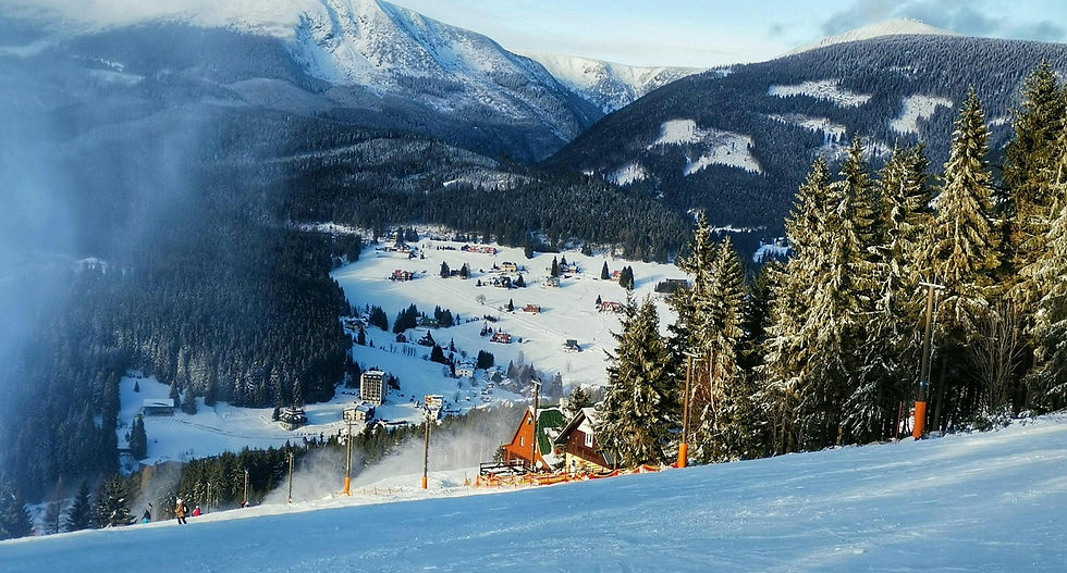 Skipiste in Tsjechië met besneeuwde bergen, naaldbossen en een winters bergdorp in het dal.