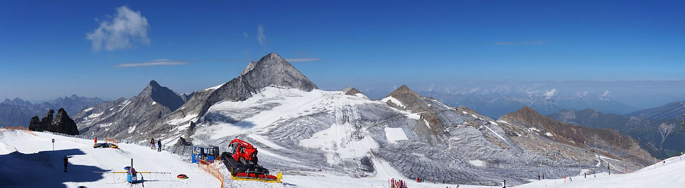 Hooggelegen skigebied met besneeuwde bergtoppen, gletsjer en skiërs onder een heldere blauwe lucht.