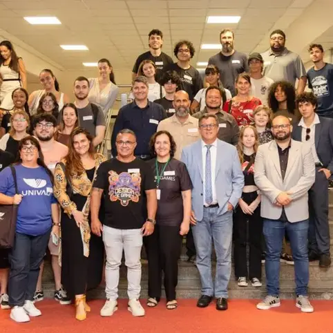 Grupo de homens e mulheres posa para foto em escadaria sobre tapete vermelho.