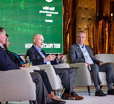 Panelists speaking on a stage at Stein Eriksen Lodge. On stage are grey armchairs and there is an LED wall beind the panelists.