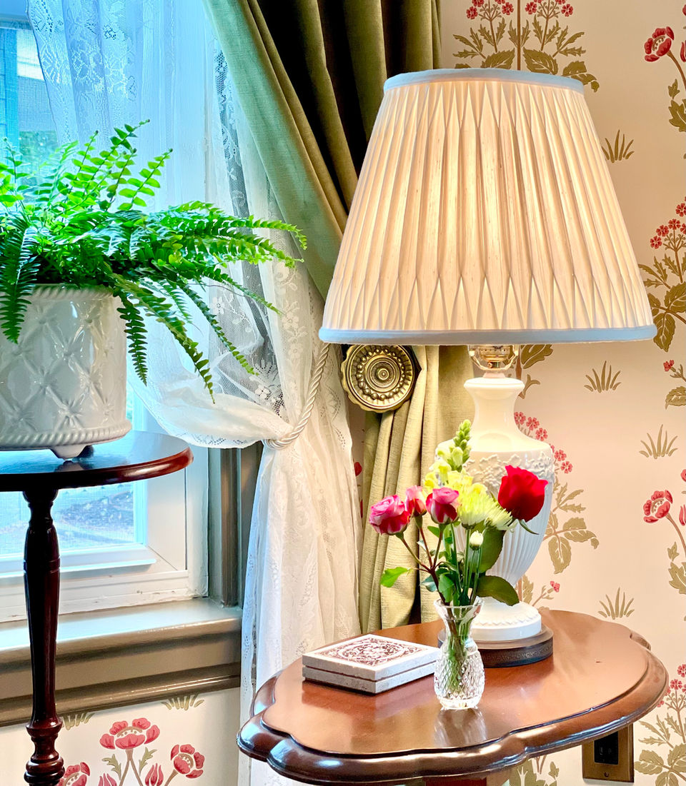 Living room with floral wallpaper, piecrust table featuring a soft beige lamp and colorful live flower posy