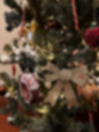 Close-up van een kerstboom bij Linden House, versierd met een gouden glitterstrik, een donutdecoratie met witte glazuurdetails, en andere kleurrijke kerstornamenten, waaronder een rode snoepstok.