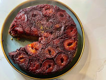 Overturned plum cake with caramelized fruit slices on a blue-rimmed plate, with a missing wedge on a white countertop.