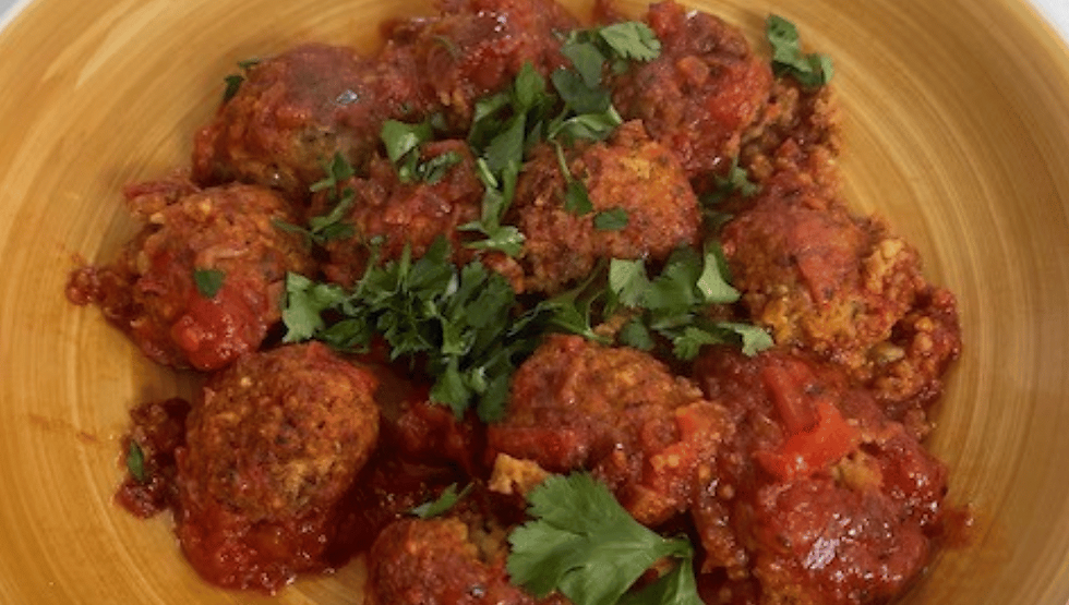 Savoury quinoa and chickpea meatballs served in a rich tomato sauce, garnished with fresh coriander for a protein-packed vegetarian meal.