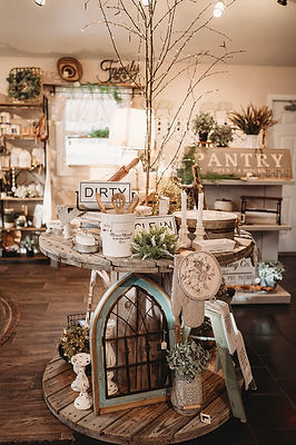 Large wooden spool used as a display table for kitchen items with a lit birch tree centerpiece at Willow & Ash Decor Co. in Shawano, WI.