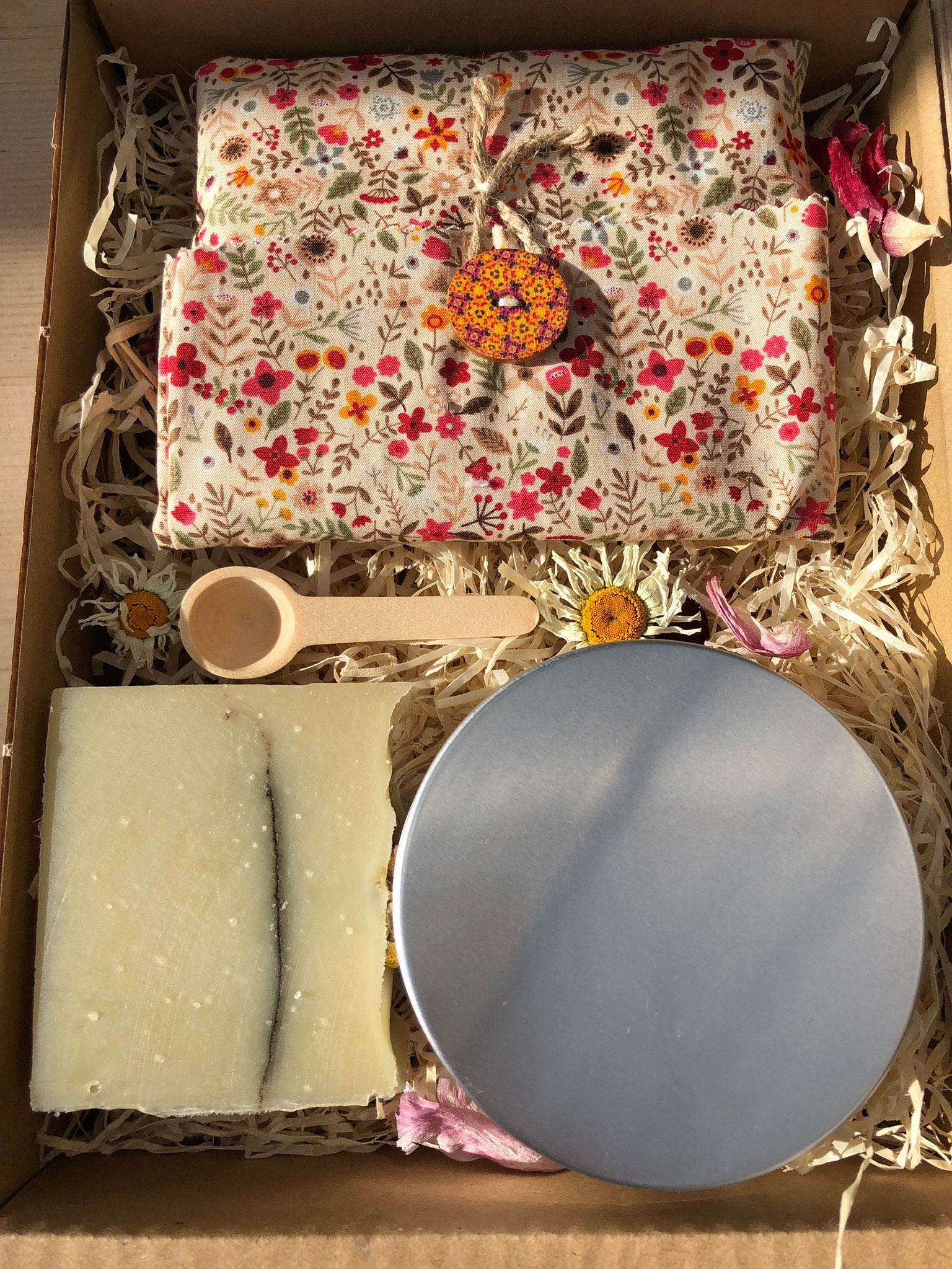 A larger gift box containing bath salts, a single soap bar chamomile and kelp , a wooden spoon and a bag of face wipes in cotton floral material.