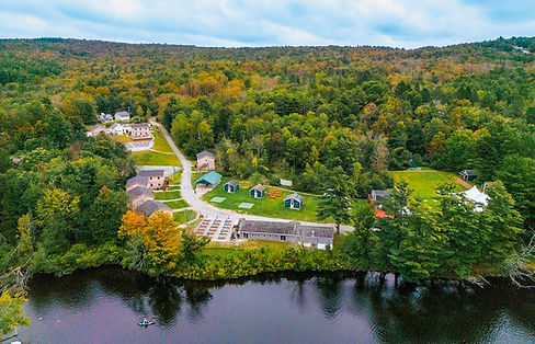Aerial of a summer camp property with a large lake, waterfront, cabins and outdoor seating
