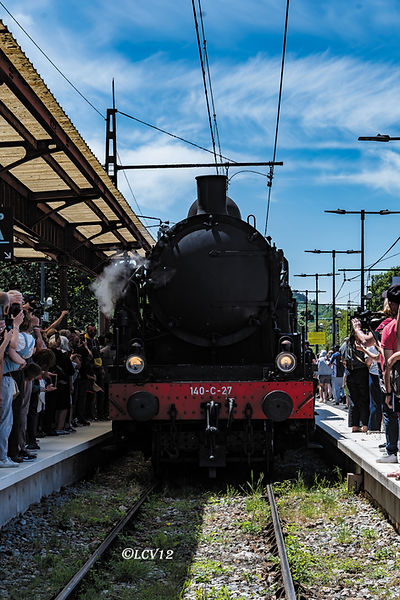 La locomotive vapeur 140 C 27 marque son arrêt en gare de Marvejols, entourée de voyageurs et passionnés venus admirer son passage.