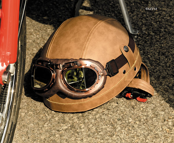 Casque moto rétro avec lunettes de pilote posé au sol dans le paddock de la Montée Classic du Viaduc à Millau.