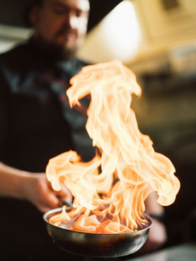 Pfanne mit Garnelen, die in der Küche flambiert werden – hohe Flammen über dem Koch.